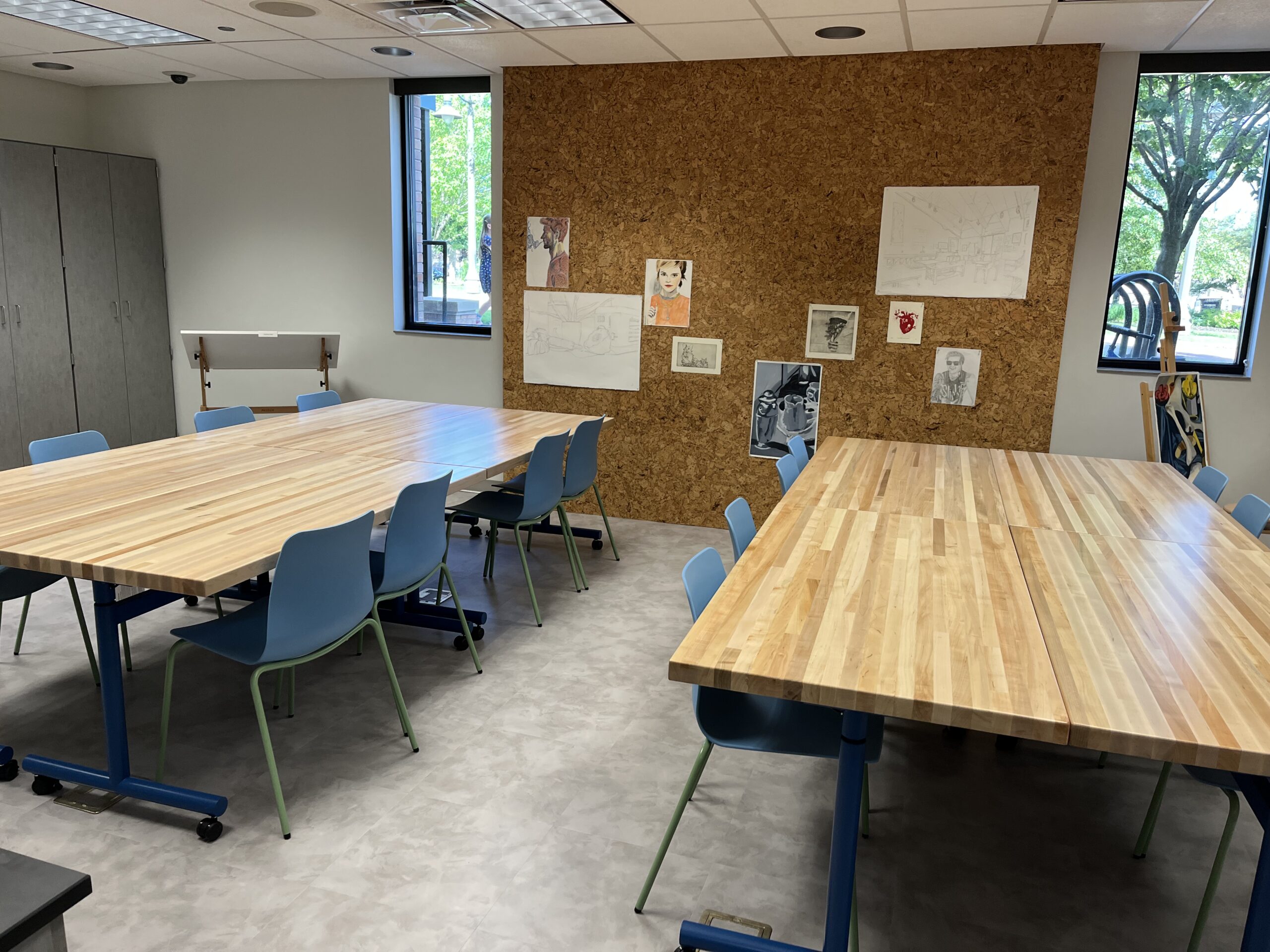 Makerspace Palette Studio grey room with a large corkboard wall filled with butcherblock tables and blue chairs.